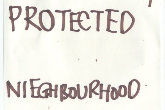 Notebook page from Step 2 with the words 'The C' crossed out, followed by 'This community protected Neighbourhood Watch' in thick black marker