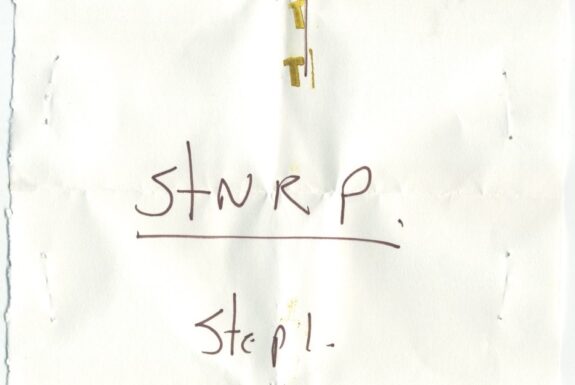 Notebook page from Step 2 with the words 'Trinity Common T STNR P Step 1' in fine black ink. The 'T' is several smaller light gold Ts stamped or stenciled over it.