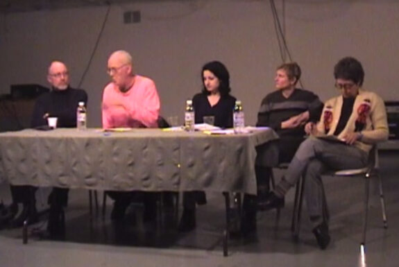Panelists Bruce Barber, Clive Robertson, Alissa Firth-Eagland, Tangy Duff and moderator Johanna Householder sit at a long table conversing as part of the panel Images versus Iconoclasms or shooting sacred cows from a train of thought, 2002