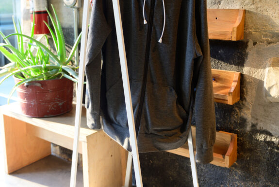 Jessica Thompson's grey DoubleBind hoodie hangs from a white clothing stand with a QR code card in front in the lobby of the Theatre Centre.